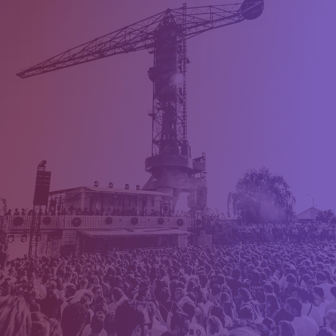 a large festival terrain with crowds and on the background a crane with a colour overlay